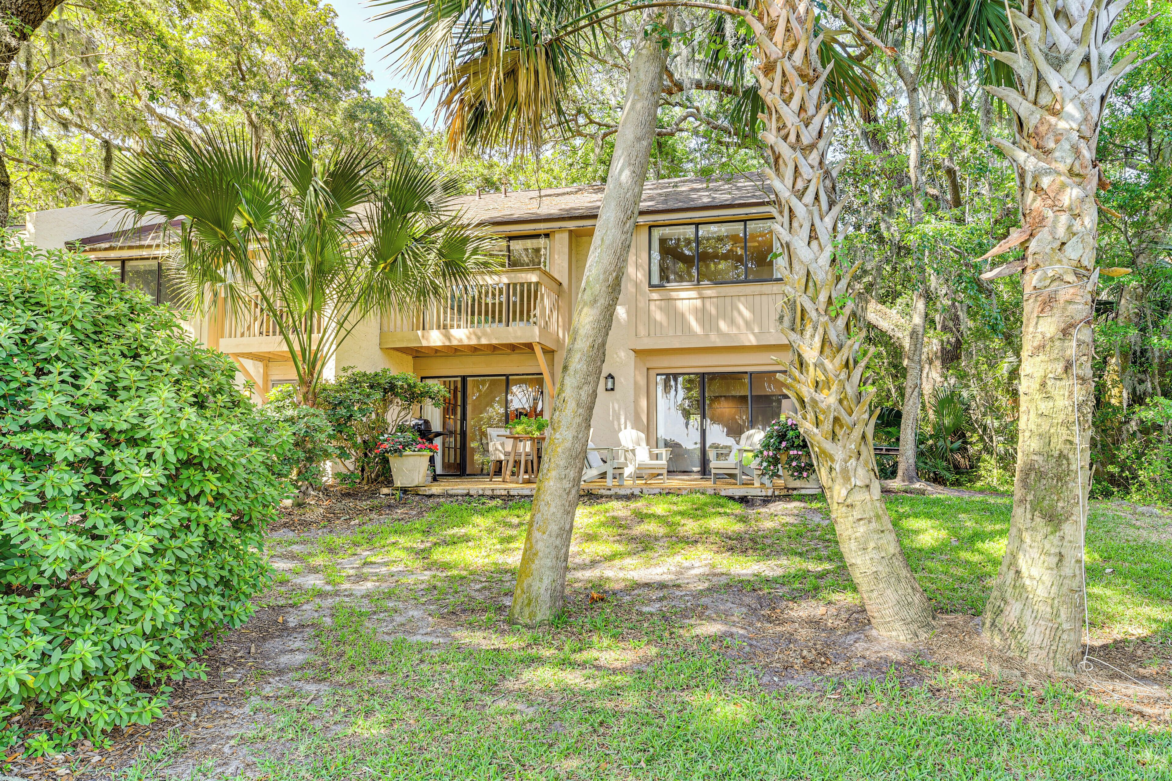 A two-story house with a balcony, surrounded by lush greenery and palm trees.