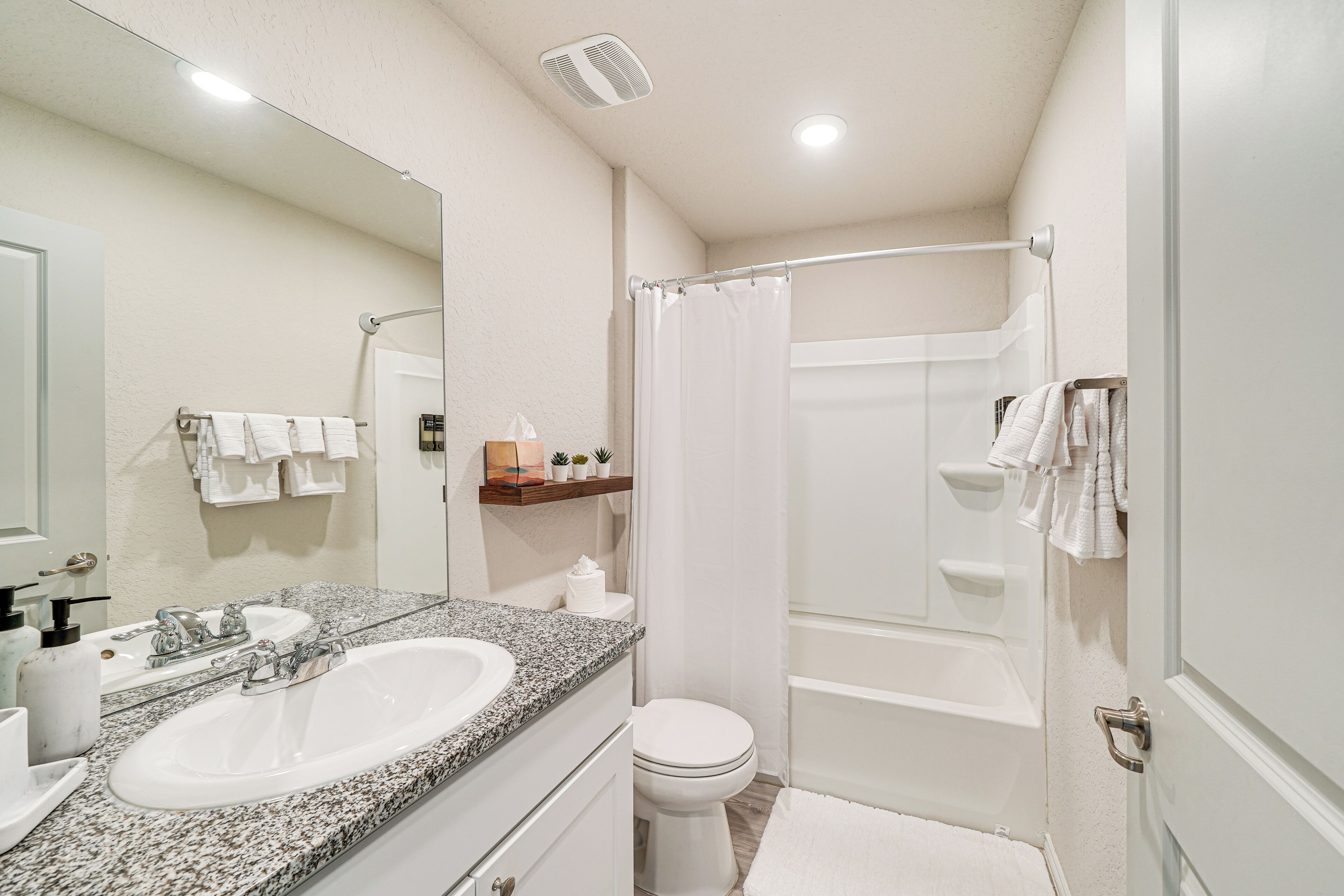 A bathroom with a granite countertop sink, a white toilet, a shower with a glass door, and a mirror above the sink.