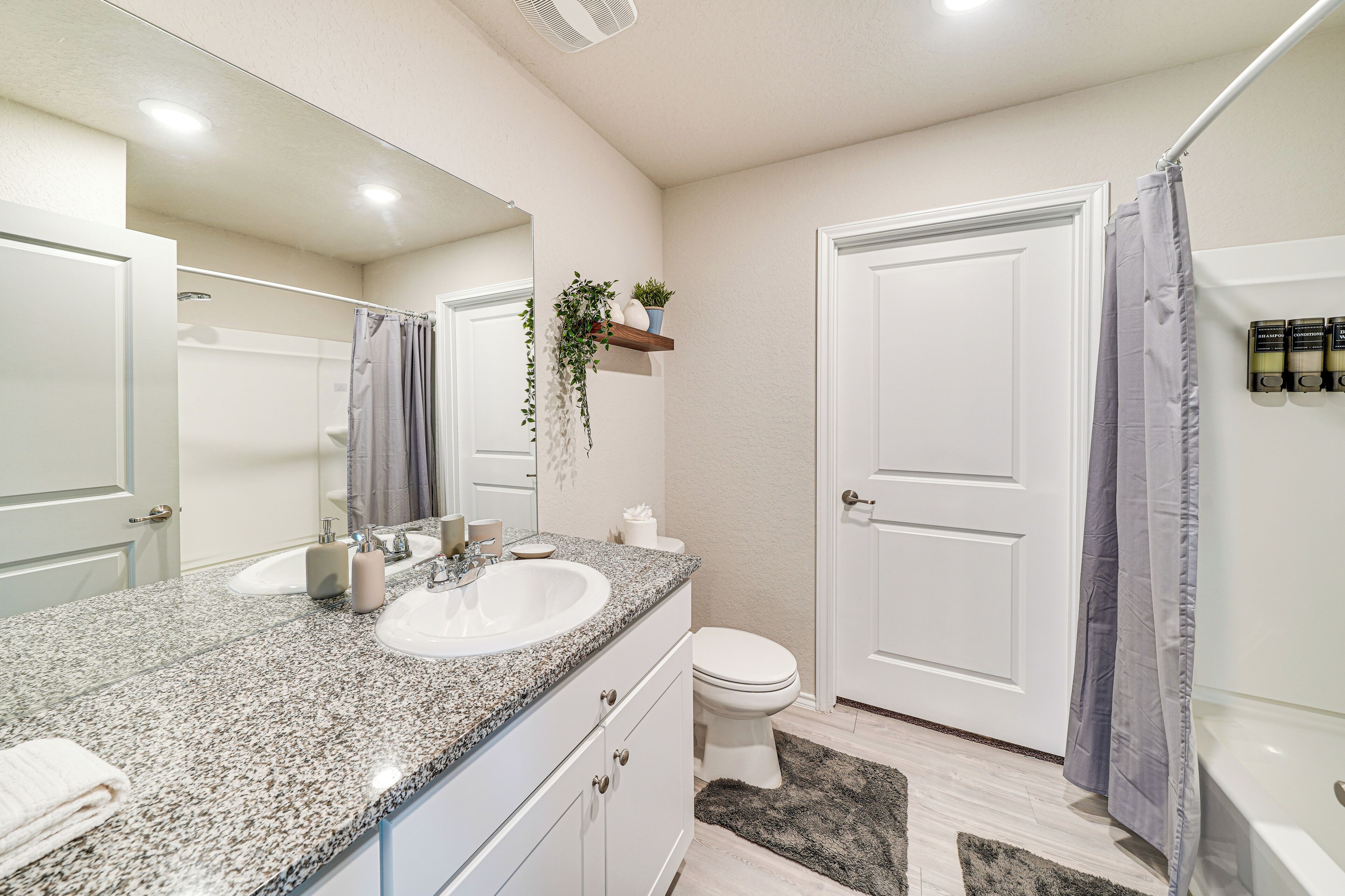 A bathroom with a granite countertop sink, a mirror, a toilet, and a shower curtain.