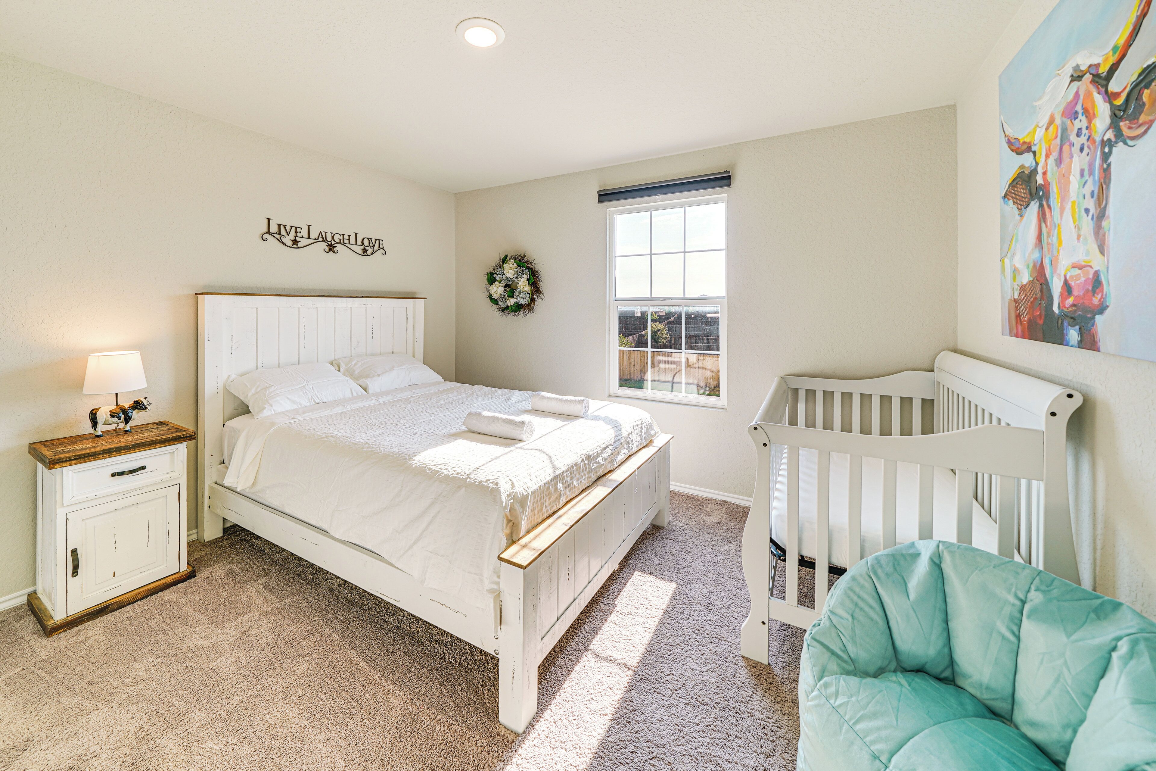 Un dormitorio con cama, cuna, mesita de noche, ventana y decoración en la pared.