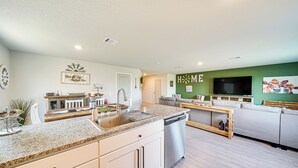 A modern kitchen with granite countertops, white cabinetry, and a dishwasher. There is a dining area with a wooden table and a green wall with the word "HOME" on it. - 10 Mi to Dtwn: Spacious San Antonio Home! (San Antonio)