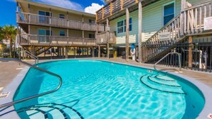 A swimming pool with a wooden deck and a multi-story building in the background. - Gulf View 23 (Gulf Shores)