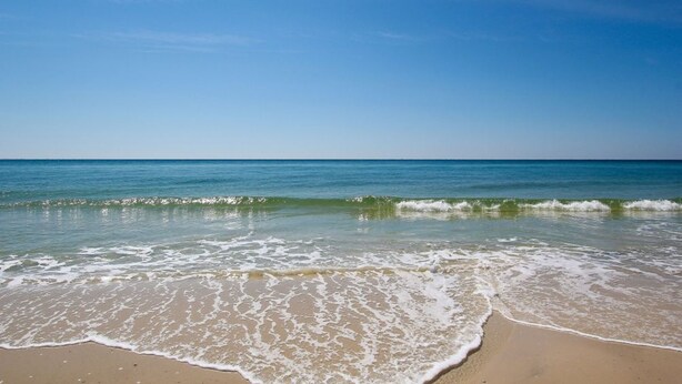 A beach with clear blue water and waves gently lapping onto the shore. - Gulf View 23 (Gulf Shores)