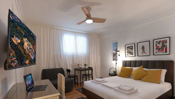 A modern hotel room with a large bed, a desk with a laptop, a ceiling fan, and artwork on the walls. - Modern Living in Kolonaki (Athens)