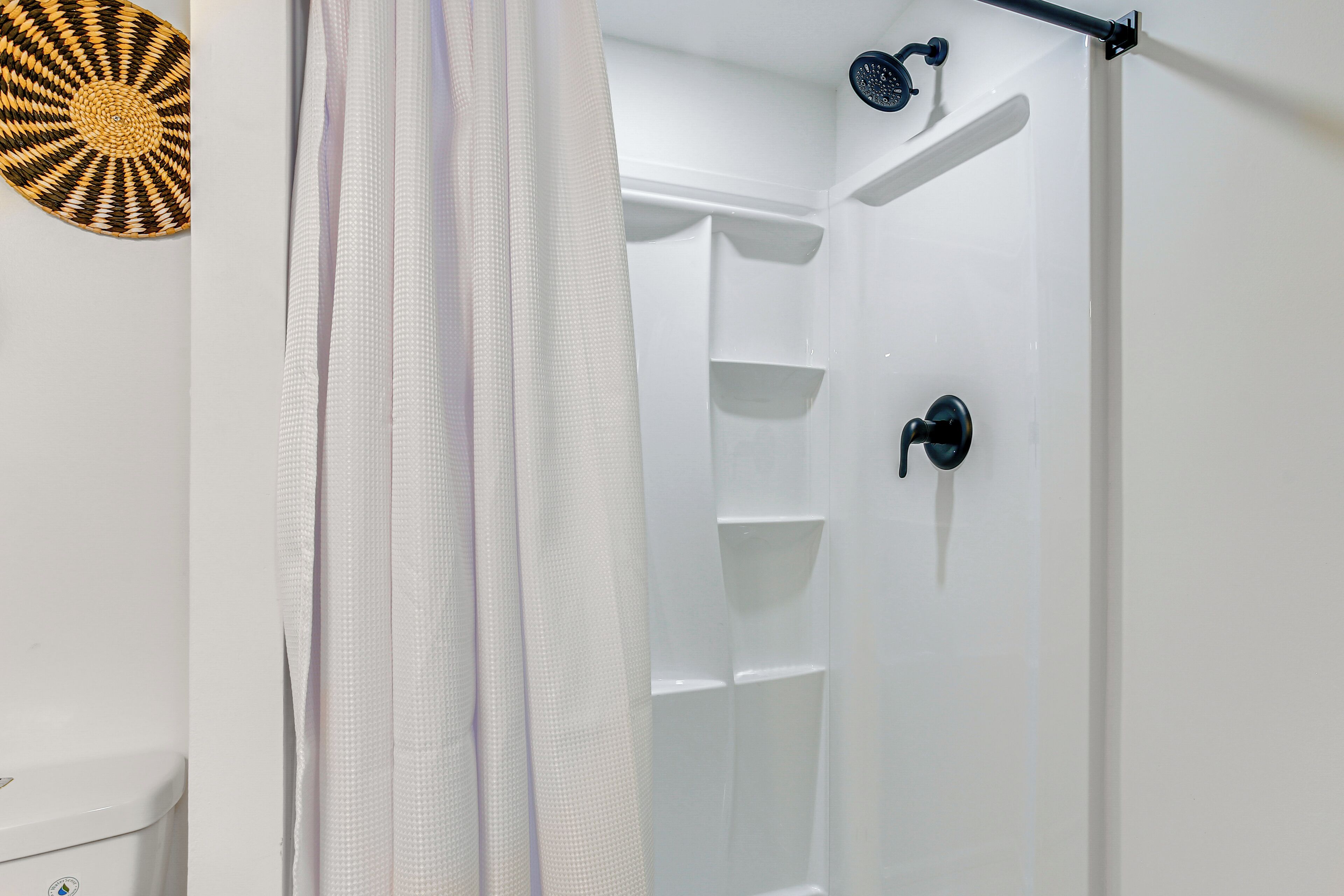 A shower with a black handle and a white shower curtain.