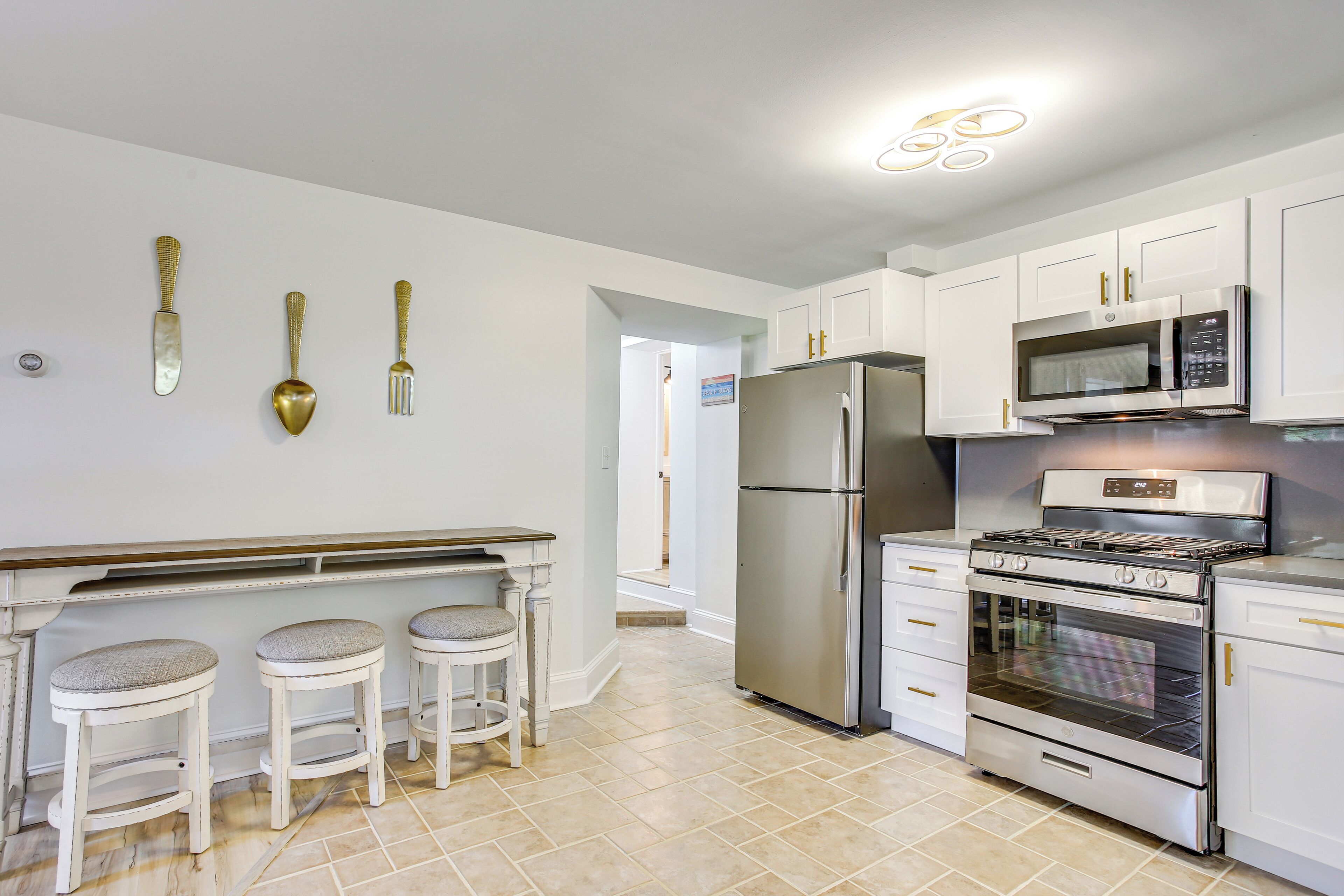 A modern kitchen with white cabinets, stainless steel appliances, and three bar stools.