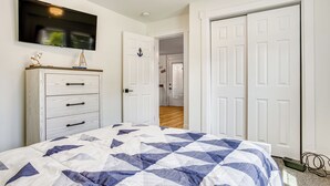 A bedroom with a bed, a dresser, a television, and a door leading to another room.
