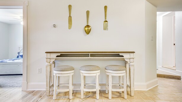 A kitchen with a white countertop, three stools, and three wall-mounted utensils.