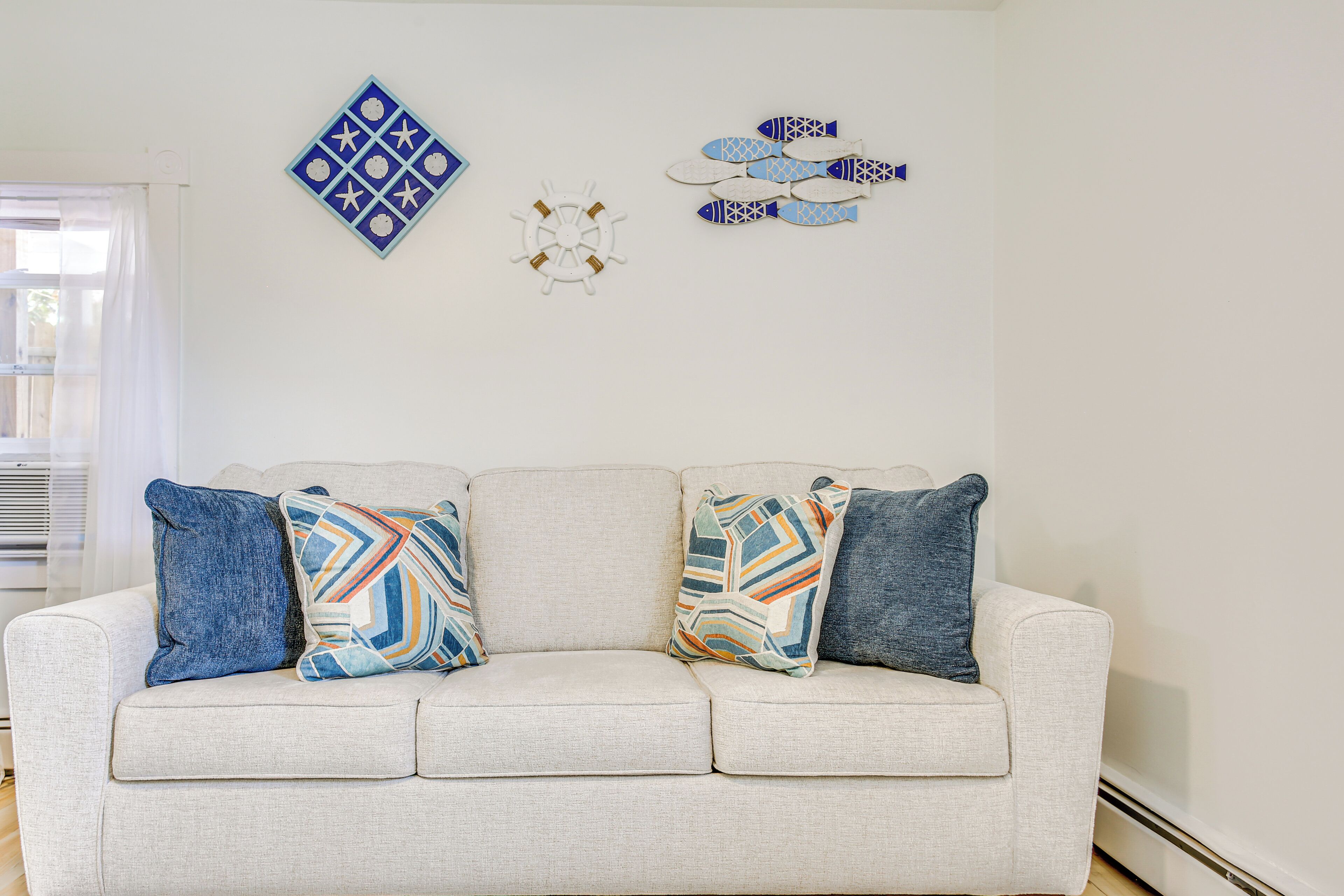 A light-colored sofa with patterned cushions, a decorative wall piece, and a geometric wall art piece.