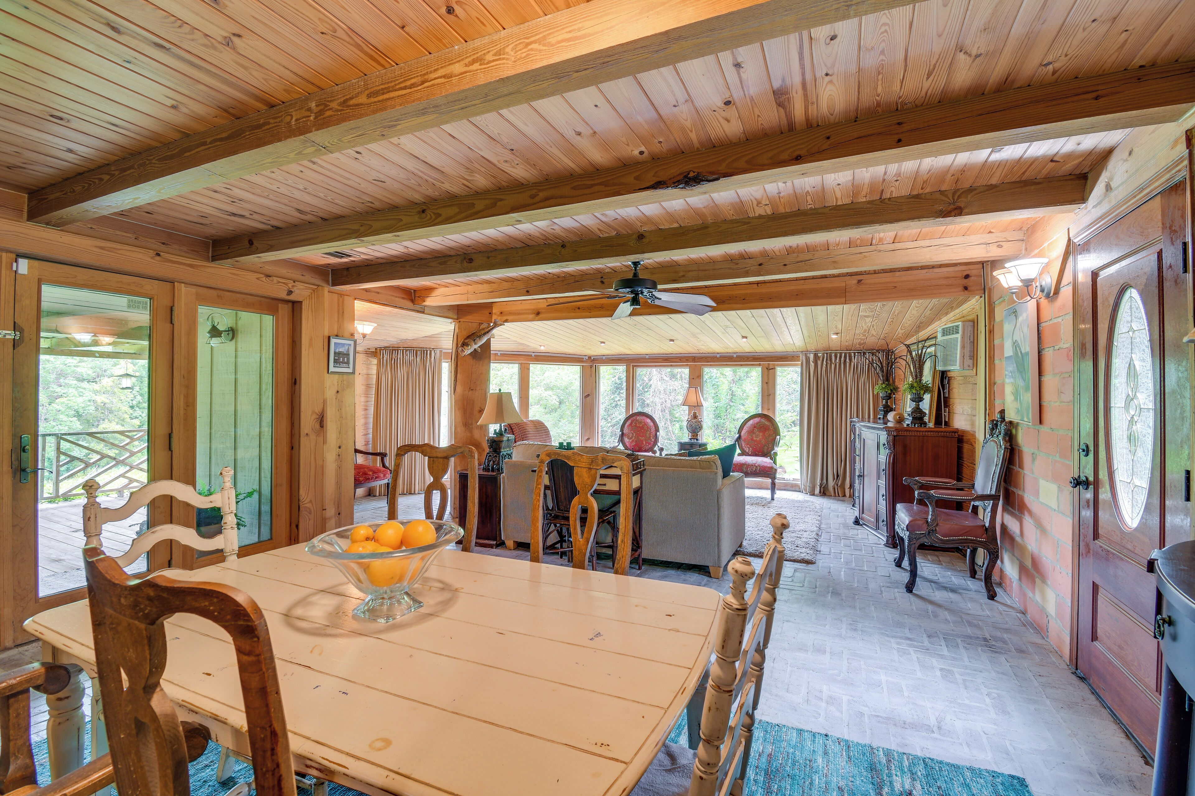 A wooden interior with a dining table, chairs, a ceiling fan, and a view through large windows.