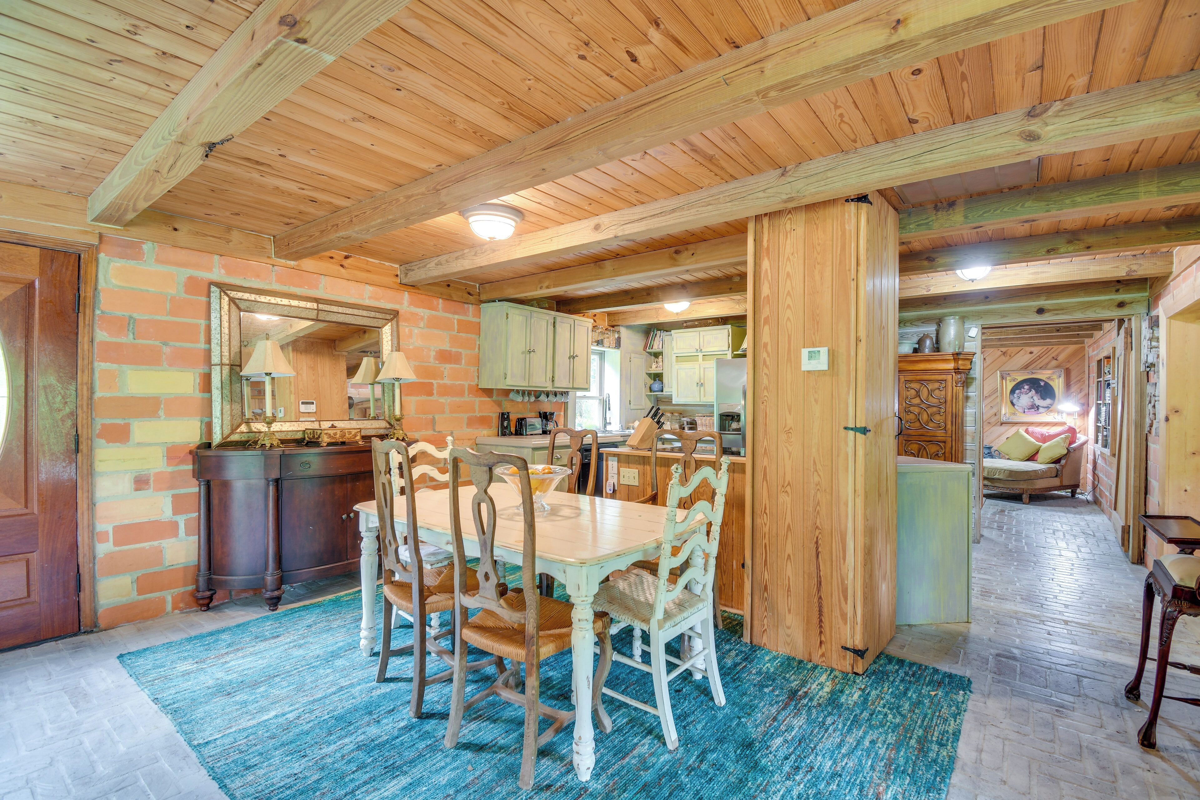 A rustic dining area with wooden tables and chairs, a brick wall, and a blue rug.