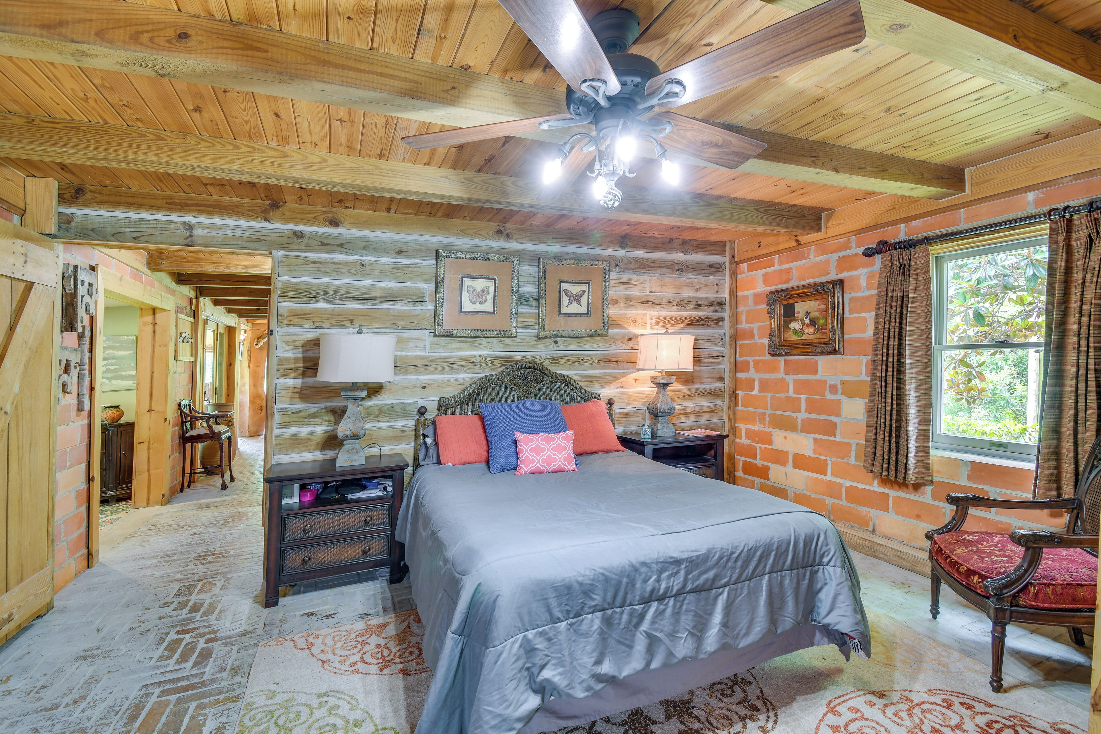 A wooden cabin bedroom with a bed, nightstands, a chair, and a window with curtains.