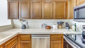 A kitchen with wooden cabinets, a dishwasher, a microwave, and various kitchen appliances and utensils on the countertop. - Escondido Townhome w/ Gas Grill + Golf Acess! (Escondido)