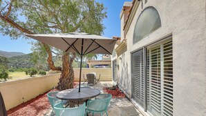 An outdoor patio with a round table and four chairs, a large umbrella, and a view of the surrounding landscape. - Escondido Townhome w/ Gas Grill + Golf Acess! (Escondido)