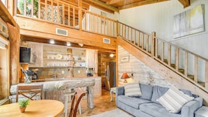 Interno di un rifugio rustico con zona pranzo, cucina e una scala che conduce a un piano superiore.