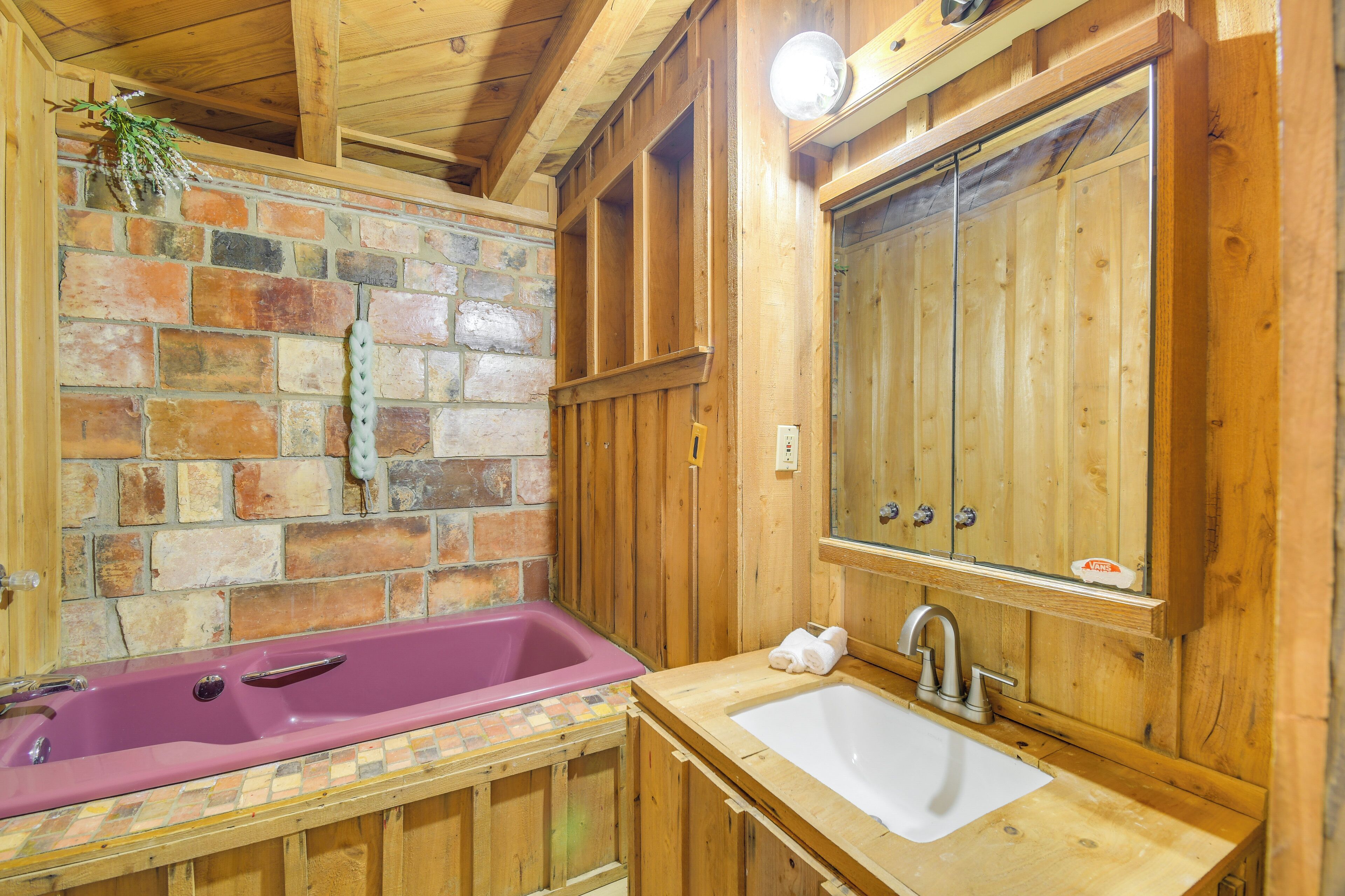A wooden cabin bathroom with a pink bathtub, a white sink, and a wooden vanity.