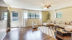 A spacious living room with hardwood flooring, a ceiling fan, a sofa set, a coffee table, and a chessboard. - Spacious Yard! Family-friendly Huntsville Home (Huntsville)