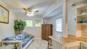A room with a wooden cabinet, a blue floral sofa, a glass table, and a ceiling fan. - Hike, Fish, Kayak: Fairhope 'river Cottage' (Fairhope)