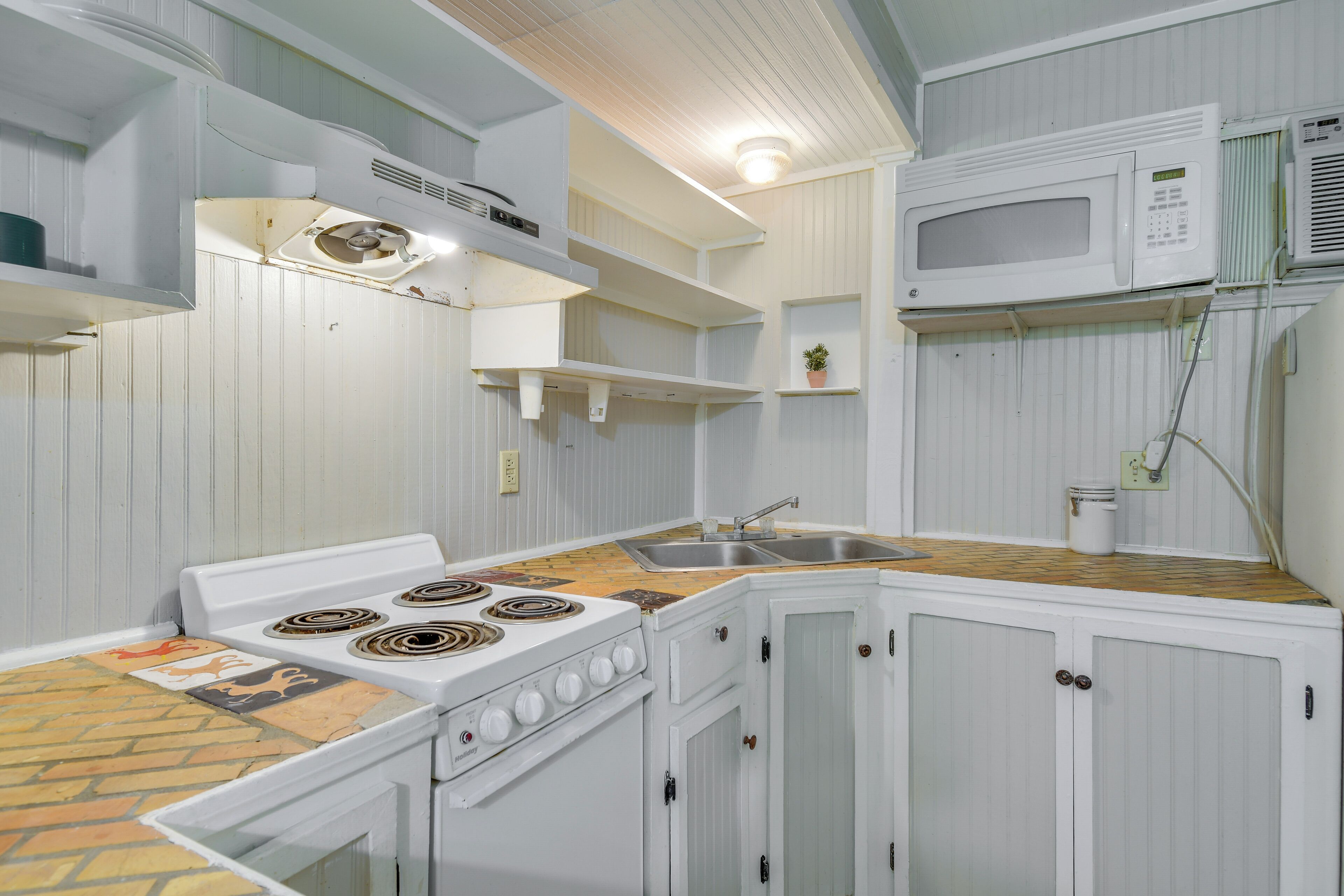 A kitchen with white cabinets, a stove, a microwave, and a sink.