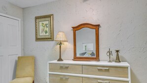 A room with a white door, a yellow chair, a wooden dresser with drawers, a framed picture, a lamp, and decorative items on the dresser. - Hike, Fish, Kayak: Fairhope 'river Cottage' (Fairhope)