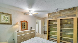 A bedroom with a bed, a dresser, a mirror, a ceiling fan, and wooden shelving. - Hike, Fish, Kayak: Fairhope 'river Cottage' (Fairhope)