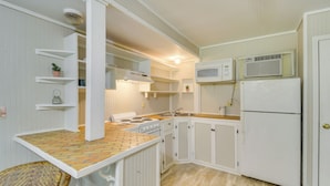 A compact kitchen with white cabinetry, a stove, a microwave, and a refrigerator. - Hike, Fish, Kayak: Fairhope 'river Cottage' (Fairhope)