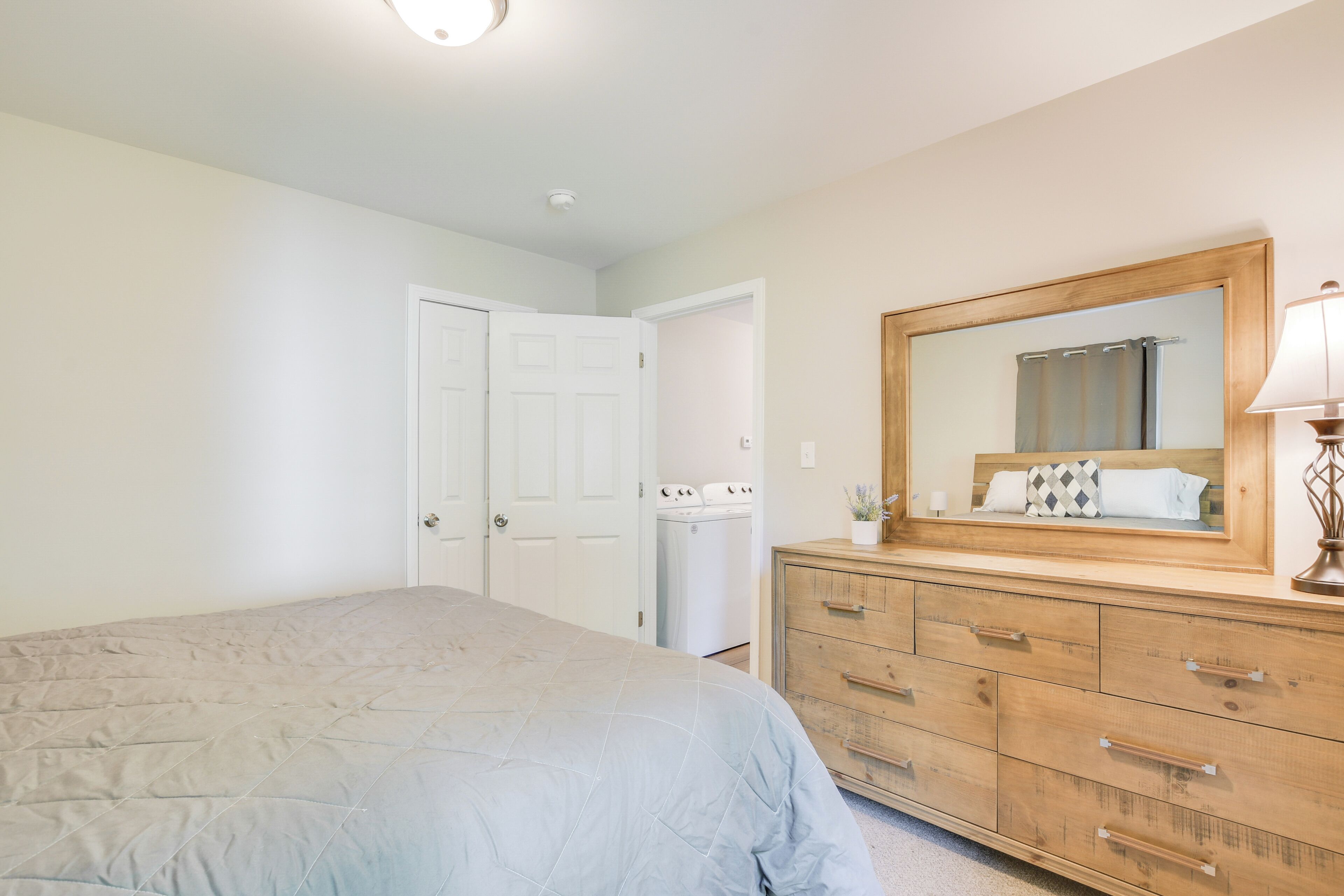 A bedroom with a bed, a wooden dresser, a mirror, and a washing machine.