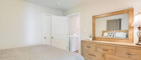 A bedroom with a bed, a wooden dresser, a mirror, and a washing machine.
