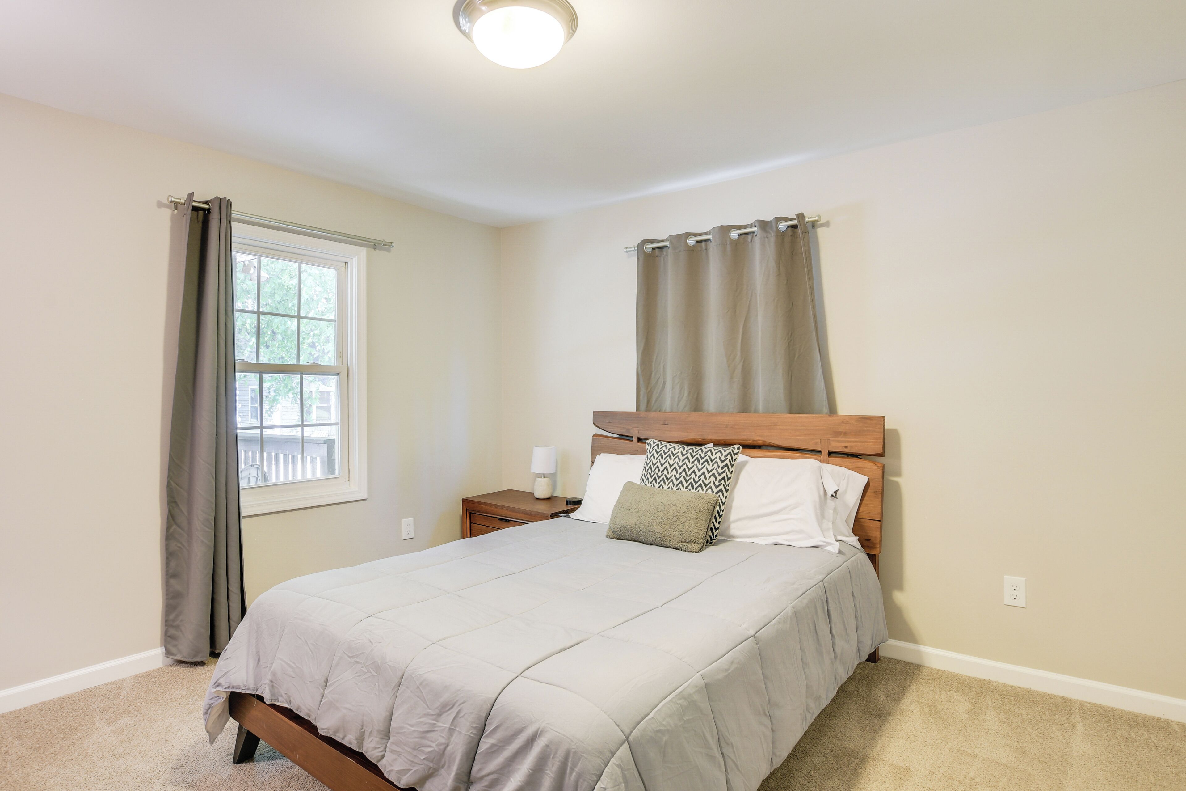 A bedroom with a bed, a nightstand, a window with curtains, and a ceiling light.