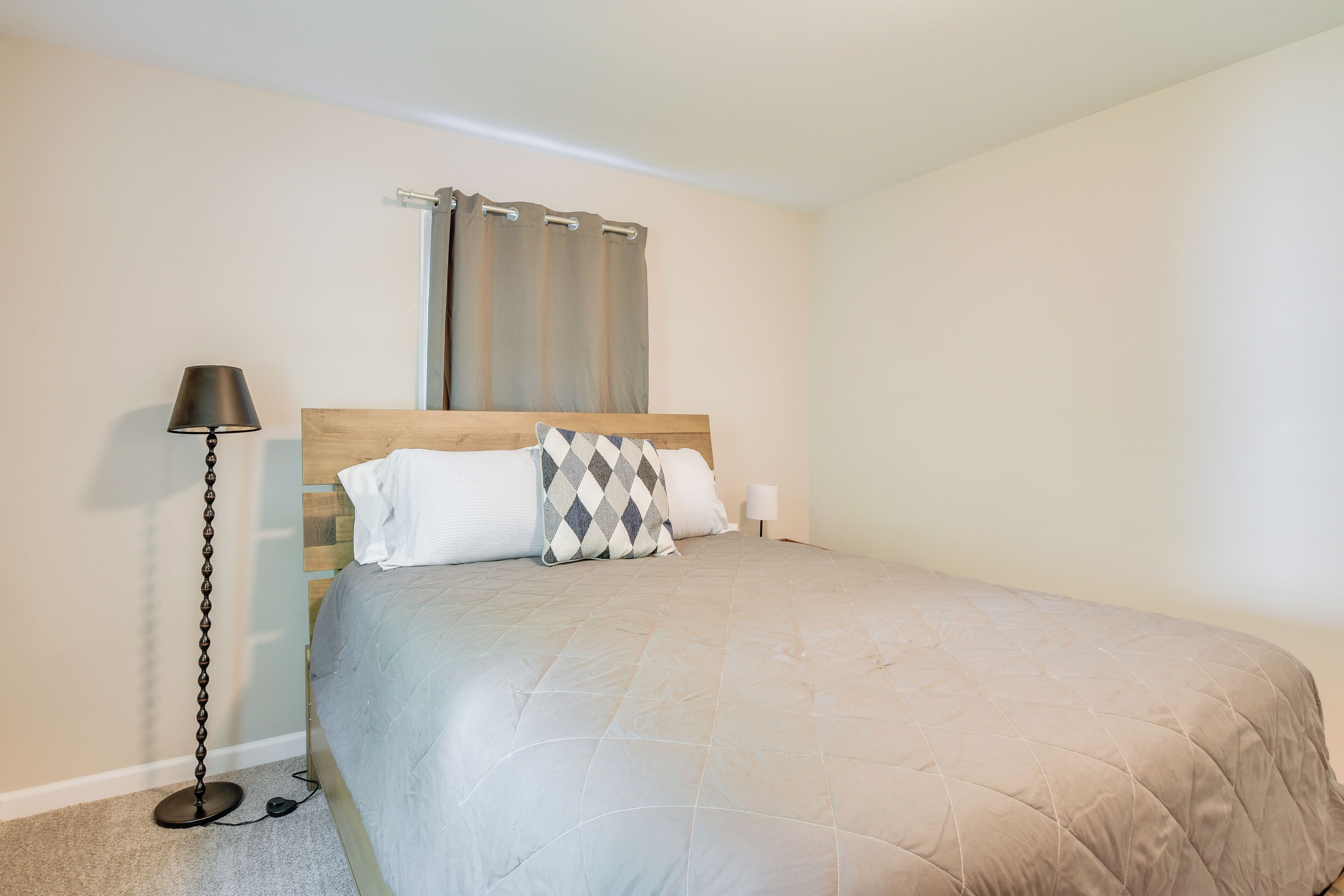 Un dormitorio con una cama, cabecera, lámpara de pie, mesita de noche y ventana con cortinas.