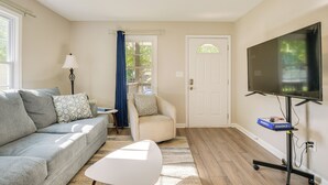 A living room with a grey sofa, a white coffee table, a TV on a stand, and a door with a window. - Charming Greenville Home w/ Yard: 3 Mi to Downtown (Greenville)
