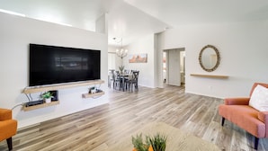 A spacious living area with a flat-screen TV mounted on the wall, a dining table with chairs, a ceiling fan, and a fireplace. - Hike, Shop & Unwind: Cottonwood Home w/ Patio! (Cottonwood)
