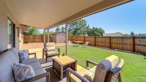A covered patio area with outdoor furniture, a small table, and a view of a backyard with a wooden fence and greenery. - Hike, Shop & Unwind: Cottonwood Home w/ Patio! (Cottonwood)