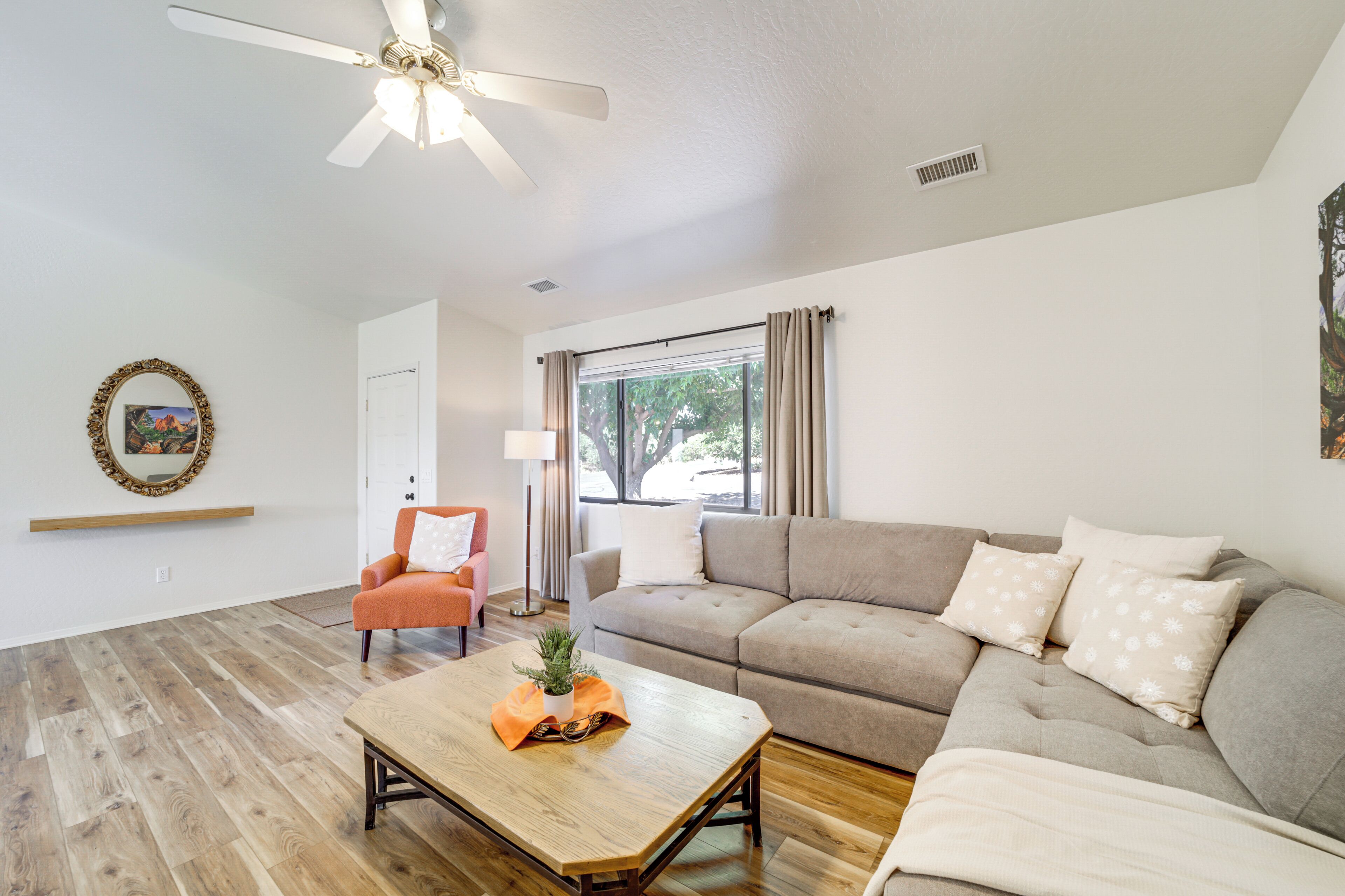 A living room with a wooden coffee table, a sofa, an orange armchair, and a ceiling fan.