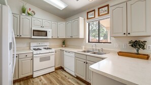 A modern kitchen with white cabinetry, a built-in microwave, a stove, and a dishwasher. There is a window with a view of trees and a wooden bench with a vase of flowers. - Hike, Shop & Unwind: Cottonwood Home w/ Patio! (Cottonwood)