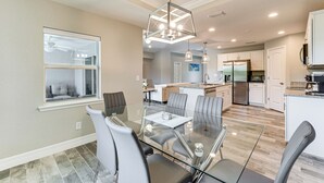 A modern kitchen with white cabinets, stainless steel appliances, and a glass dining table. - South Gulf Cove Retreat w/ Grill - 13 Mi to Beach! (Port Charlotte)