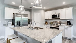 A modern kitchen with white cabinets, stainless steel appliances, a granite countertop, and bar stools. - South Gulf Cove Retreat w/ Grill - 13 Mi to Beach! (Port Charlotte)