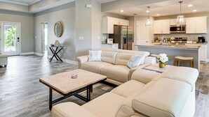 A spacious living room with a beige sectional sofa, a coffee table, and a dining area with a kitchen in the background. - South Gulf Cove Retreat w/ Grill - 13 Mi to Beach! (Port Charlotte)