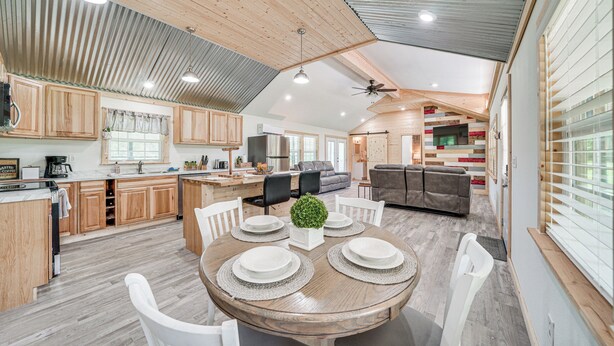 A spacious kitchen with wooden cabinets, a dining area with a round table set for four, and a living area with a sofa and TV. - Secluded Broken Bow Cabin w/ Fishing Pond & Views! (Broken Bow)