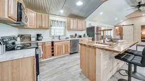 A modern kitchen with wooden cabinets, a central island with bar stools, stainless steel appliances, and a ceiling fan. - Secluded Broken Bow Cabin w/ Fishing Pond & Views! (Broken Bow)