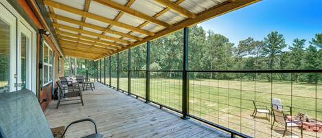 A covered outdoor deck with wooden flooring and metal railings, overlooking a grassy area with trees.