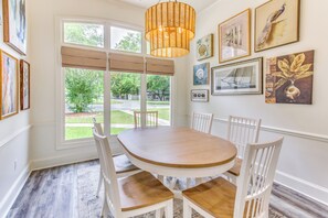 Un coin repas avec une table ronde en bois, des chaises blanches et un luminaire suspendu en fibres tressées.