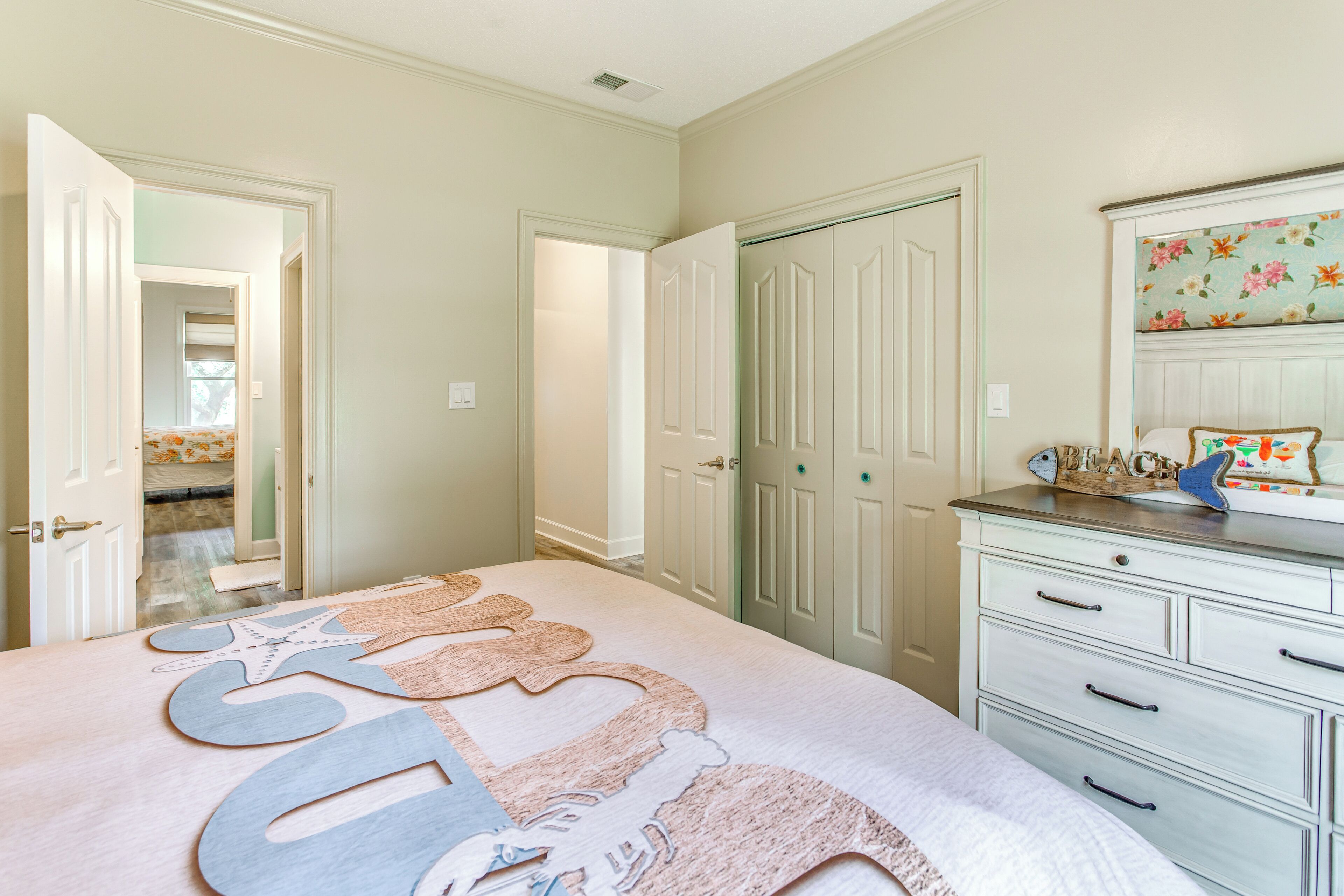 A bedroom with a large bed, a dresser, and a door leading to another room.