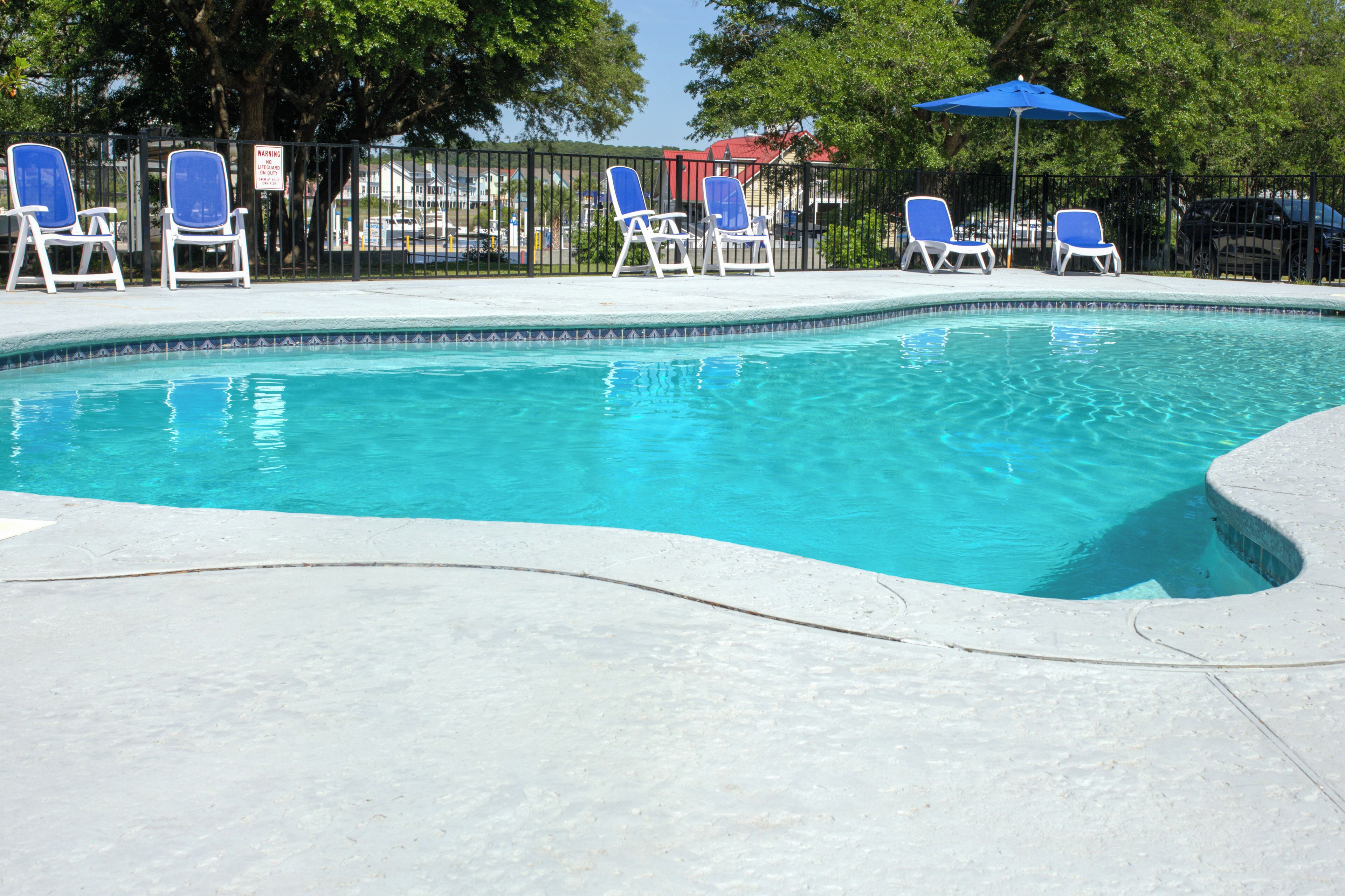 A swimming pool with blue chairs and a fence.