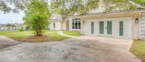 A two-story house with a brick driveway, a small tree, and a well-maintained lawn.