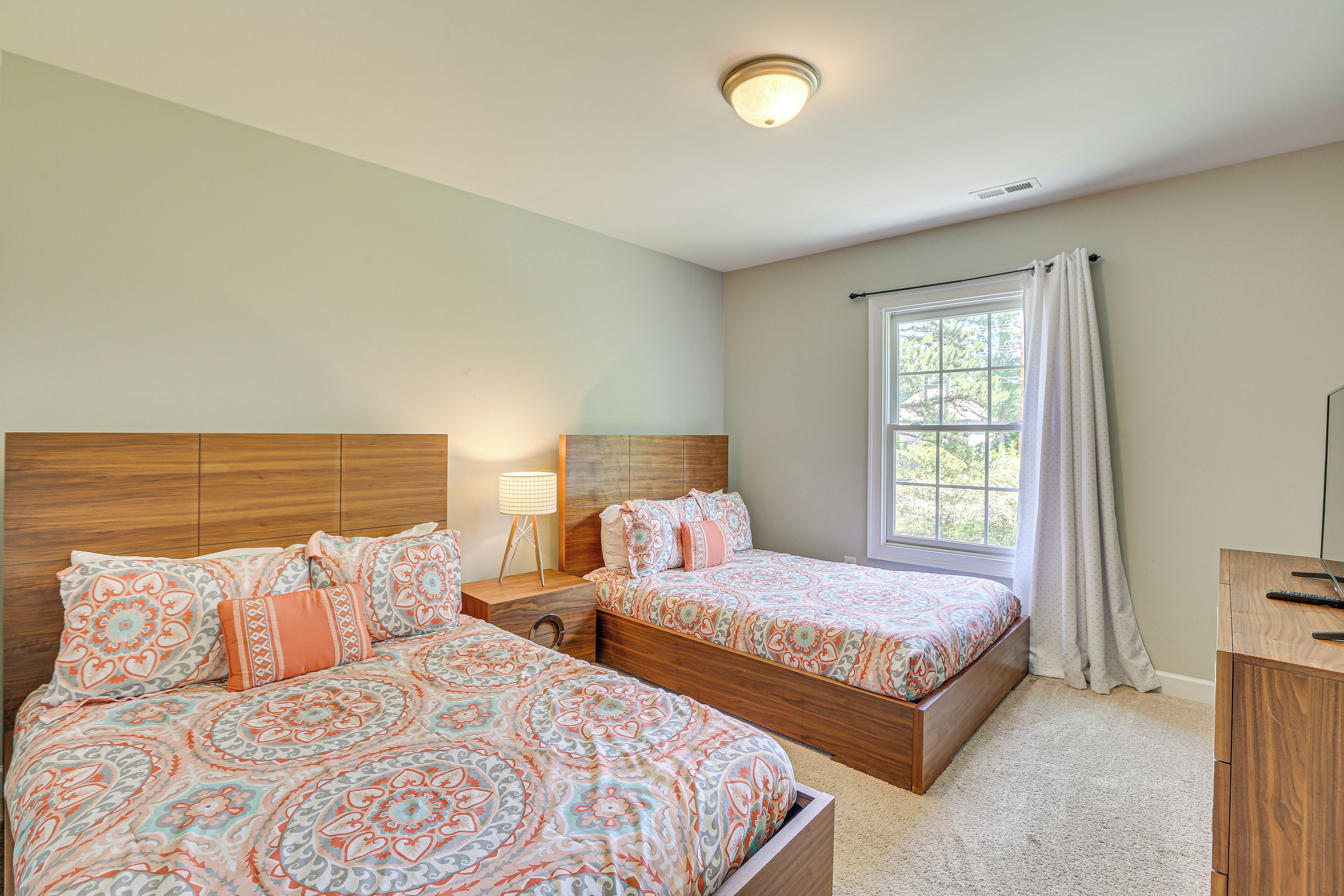 A bedroom with two beds, a nightstand, a desk, and a window with curtains.