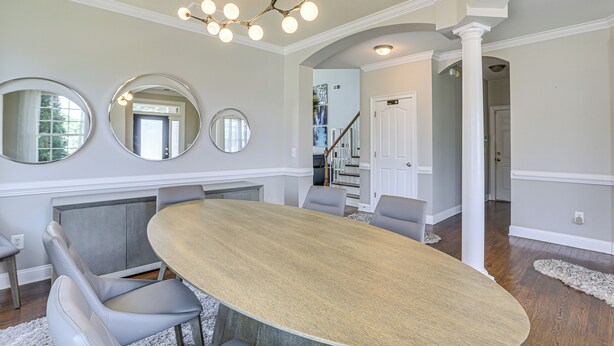 Een eetgedeelte met een grote ovale tafel, grijze bekleden stoelen en drie ronde spiegels aan de muur.