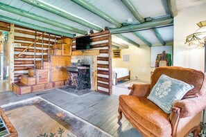 L’intérieur d’un chalet rustique en rondins de bois, avec un escalier en bois, une cheminée, un lit en bois et un fauteuil confortable agrémenté d’un coussin.