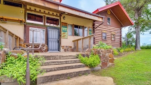 A wooden log cabin with a stone staircase leading to the entrance, surrounded by greenery.