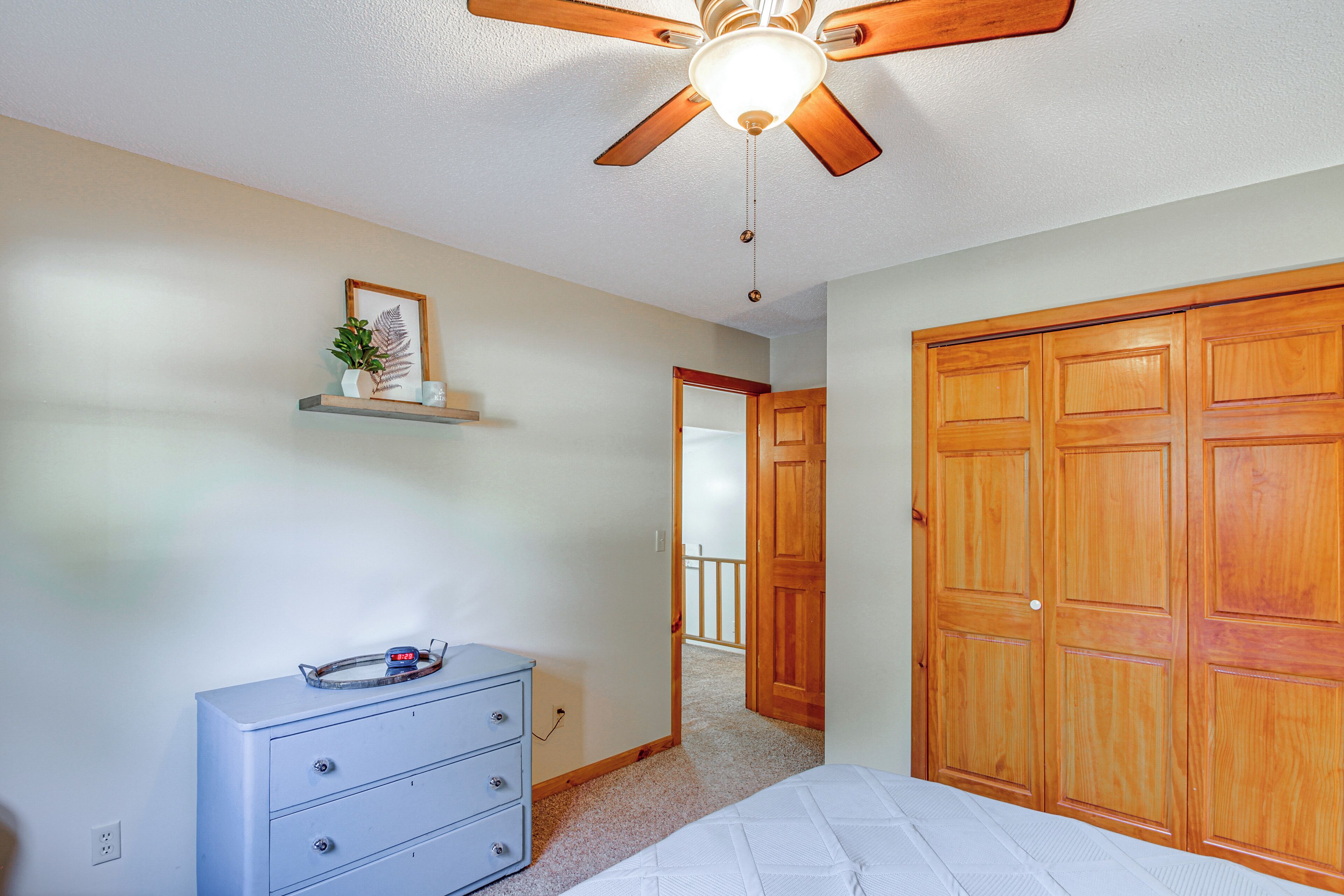 Une chambre à coucher avec un ventilateur de plafond, une commode, un lit et des portes en bois.